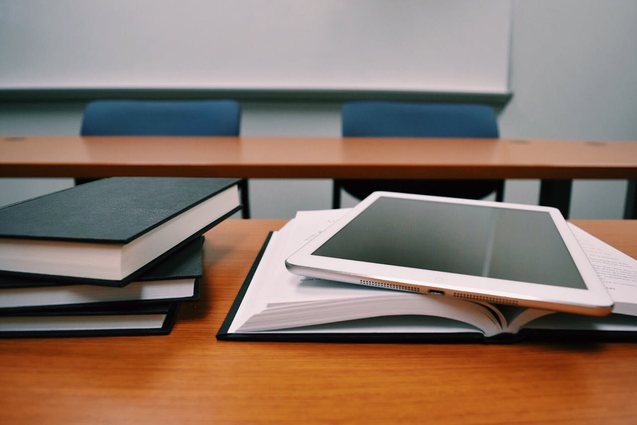 Books and a tablet on a desk in a classroom, depicting modern education.